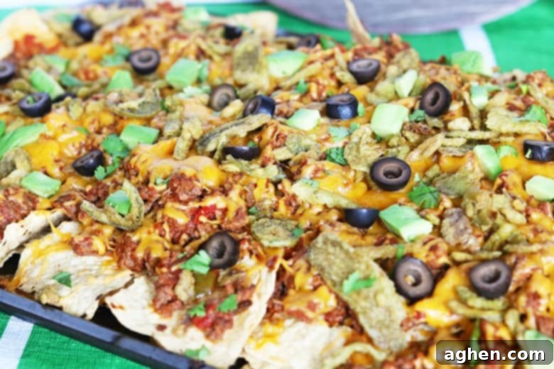 Loaded nachos on a sheet pan topped with cheese, beef, olives, cilantro, and avocado.