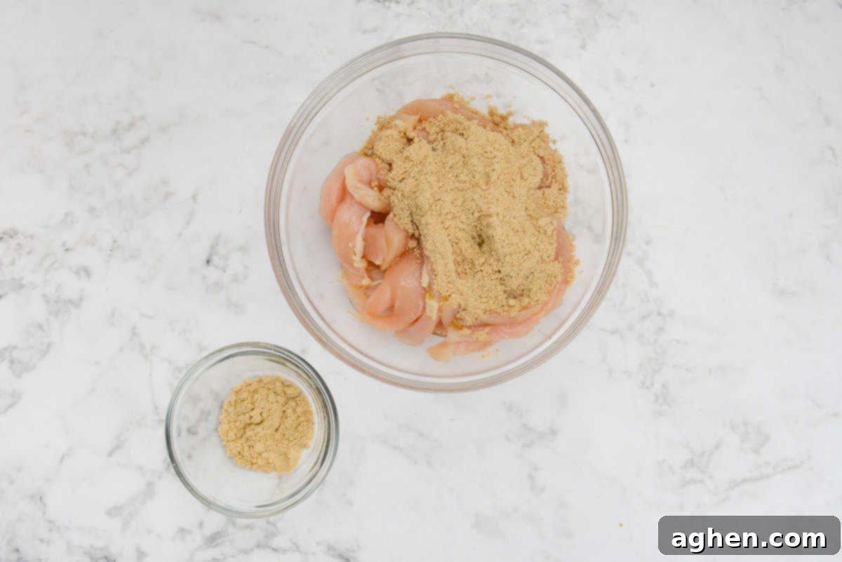 A bowl filled with sliced chicken is covered with a sprinkling of fajita seasoning. A small prep bowl of the reserved seasoning sits to the side.