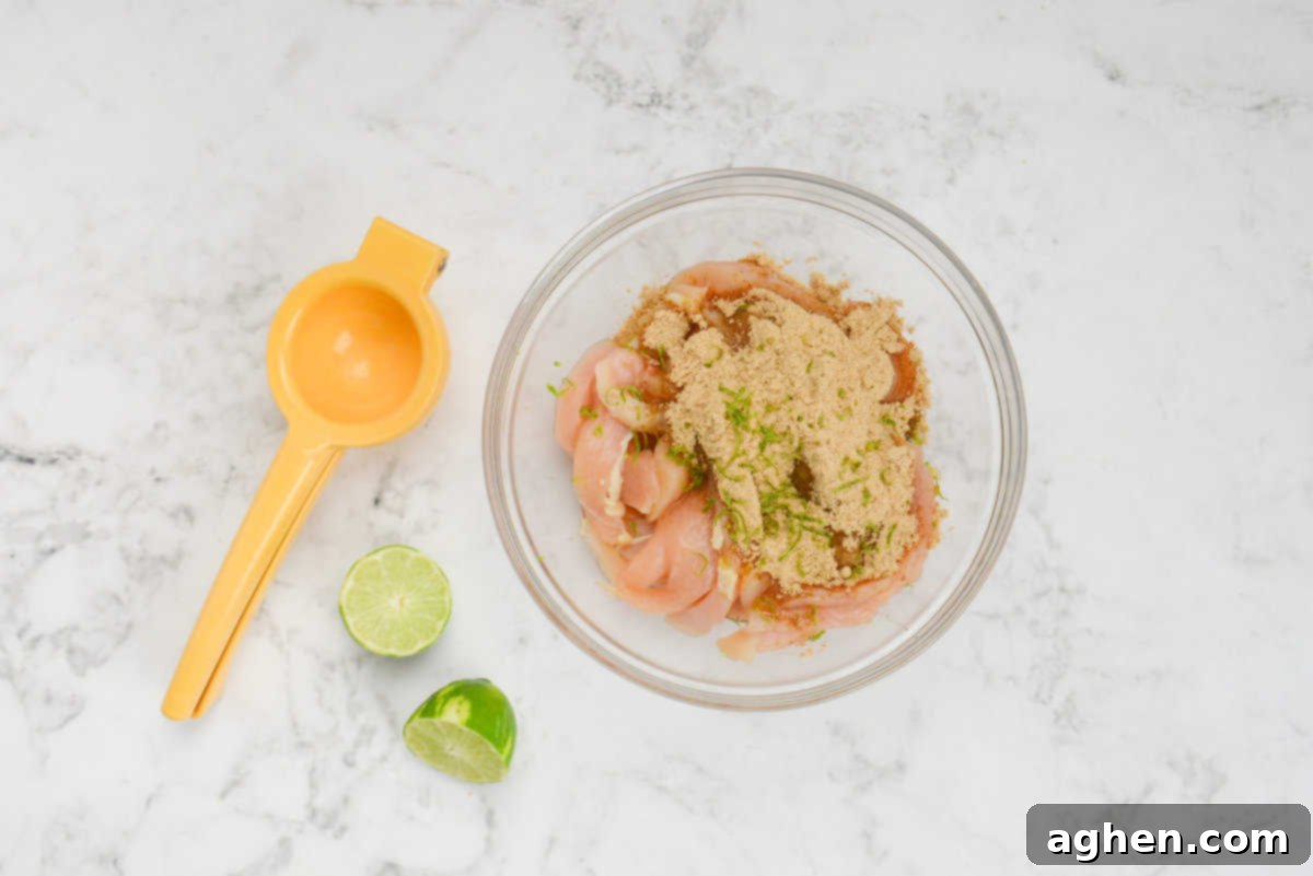 A bowl filled with sliced chicken is topped with fajita seasoning and fresh lime zest. To the left is a hand held juicer and a lime cut in half.