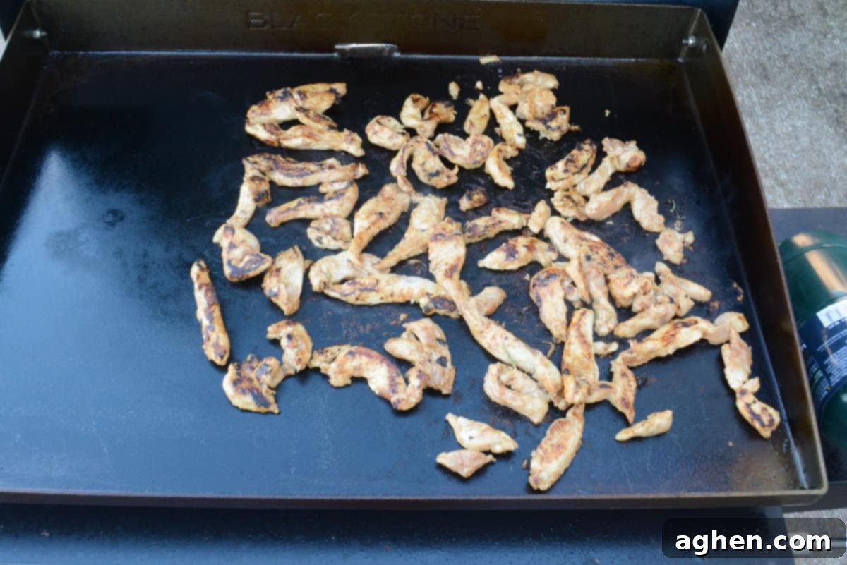 Strips of chicken sit on top of the Blackstone and are now golden brown with dark char marks 