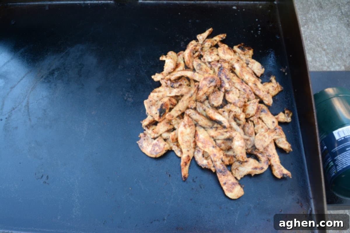 Cooked chicken scooped in a pile sits on the right side of the Blackstone 