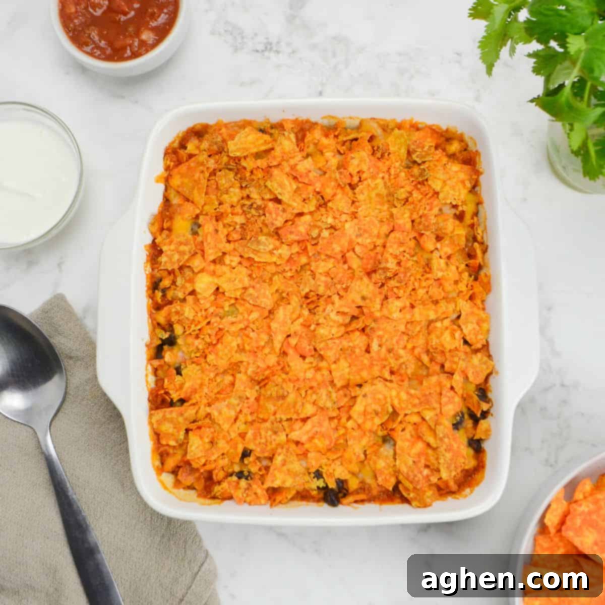 Indulge in Doritos Casserole on Weight Watchers! 2 A white square baking dish filled with Doritos casserole sits on a white table. Surrounding it are small bowls of Greek yogurt, salsa, cilantro, and Doritos. A serving spoon on a brown napkin sits to the side.