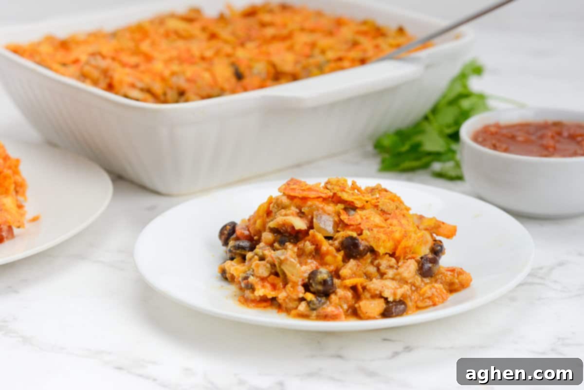 Indulge in Doritos Casserole on Weight Watchers! 14 A small white plate is filled with a serving of Doritos Casserole. The baking dish and a small bowl of salsa are shown behind the plate.