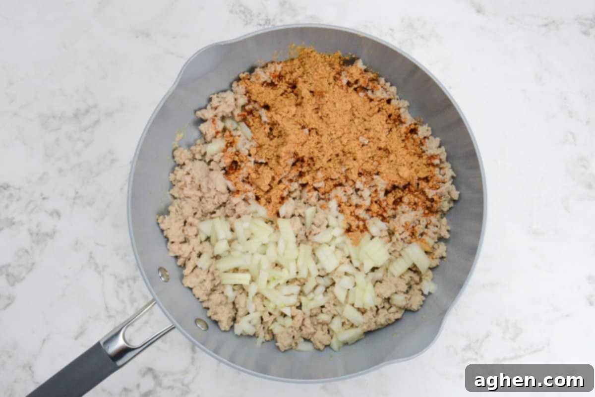 Indulge in Doritos Casserole on Weight Watchers! 4 A skillet with cooked light brown ground chicken, taco seasoning and diced onions.