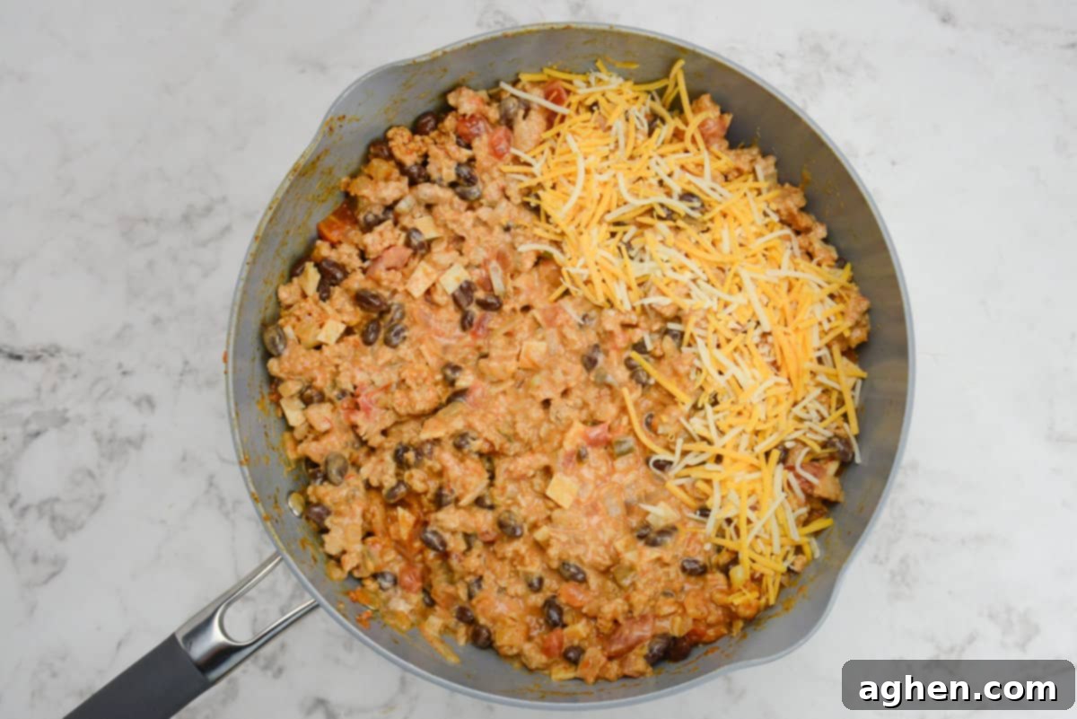 Indulge in Doritos Casserole on Weight Watchers! 9 A skillet is shown with the casserole ingredients mixed well with a portion of orange and white cheese on top.