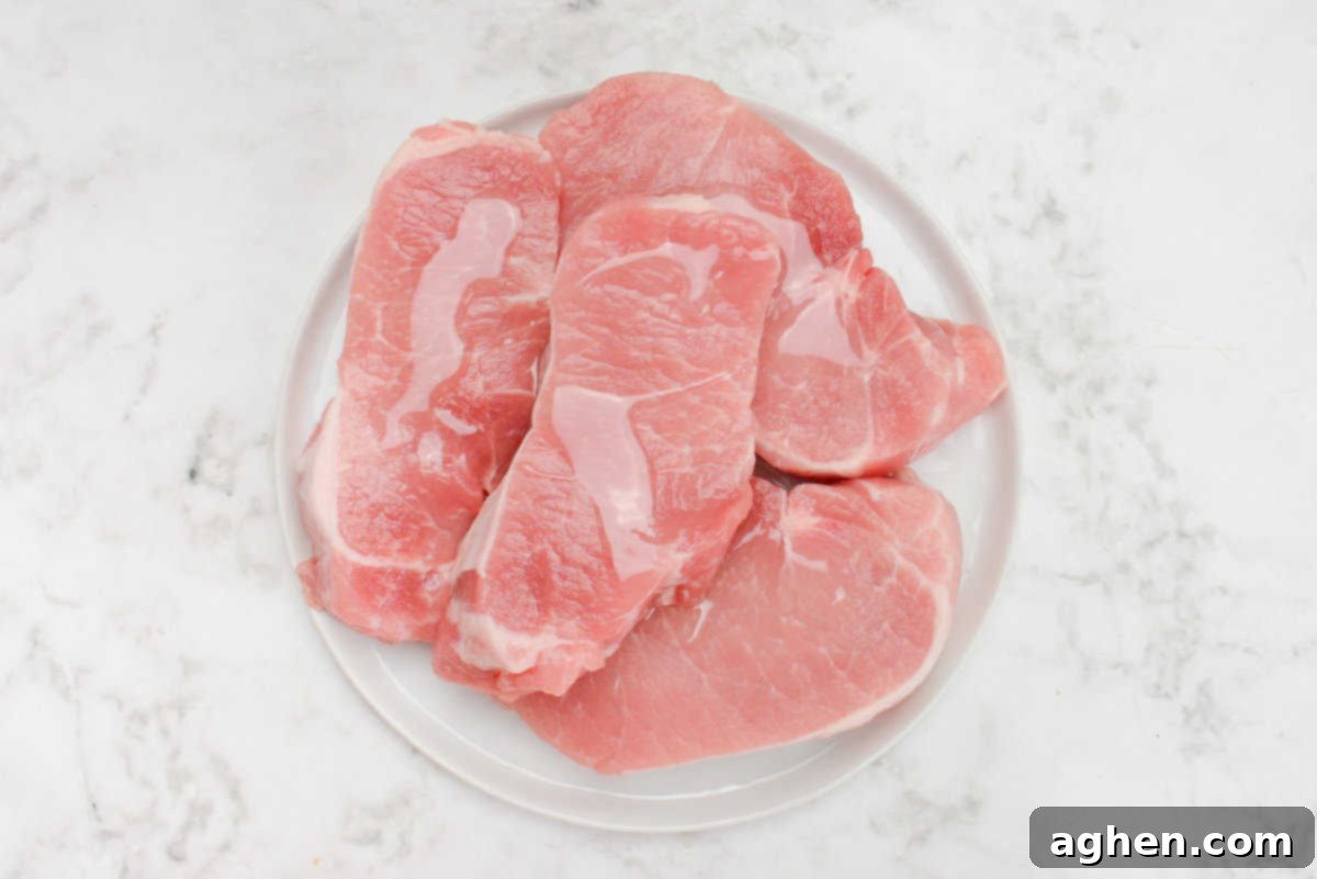 Blackstone'da Domuz Pirzolası 7 Kolay Adımda 6 raw pork chops being drizzled with olive oil on a plate
