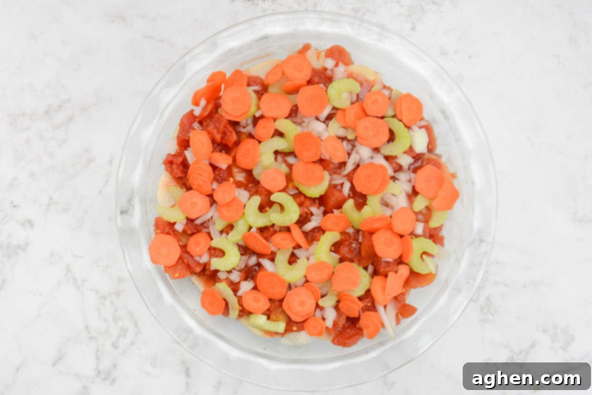 A pie plate showcases the addition of vibrant carrots and chopped celery, creating another colorful and textural layer on top of the tomatoes and onions.