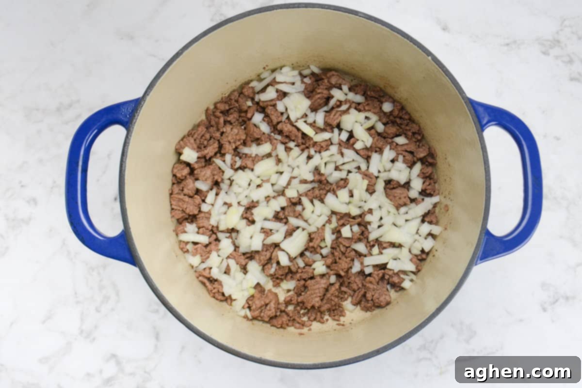 Guilt-Free Cowboy Casserole: A Weight Watchers Recipe You'll Love 5 A blue Dutch oven is shown with a layer of beef topped with onions.