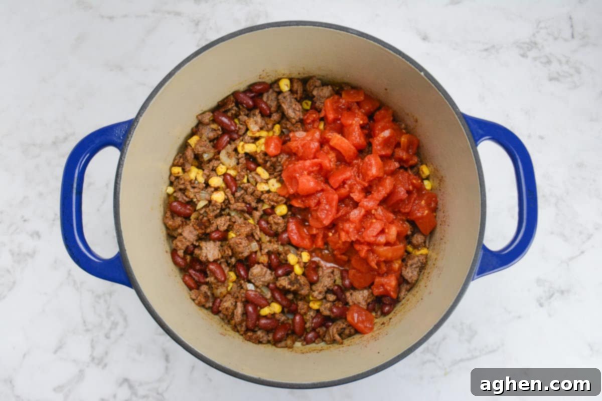 Guilt-Free Cowboy Casserole: A Weight Watchers Recipe You'll Love 7 A blue Dutch oven is shown with the mixed beef mixture and vibrant tomatoes on top.