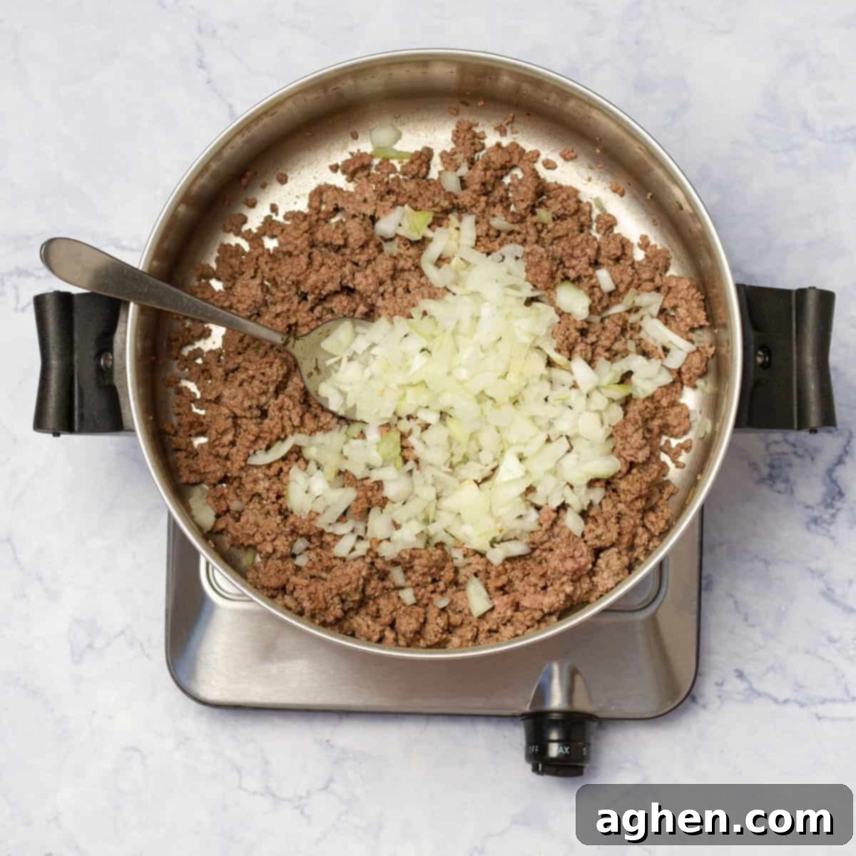 Finely chopped onion and crushed garlic added to browned ground beef in a pot, sautéing until fragrant.