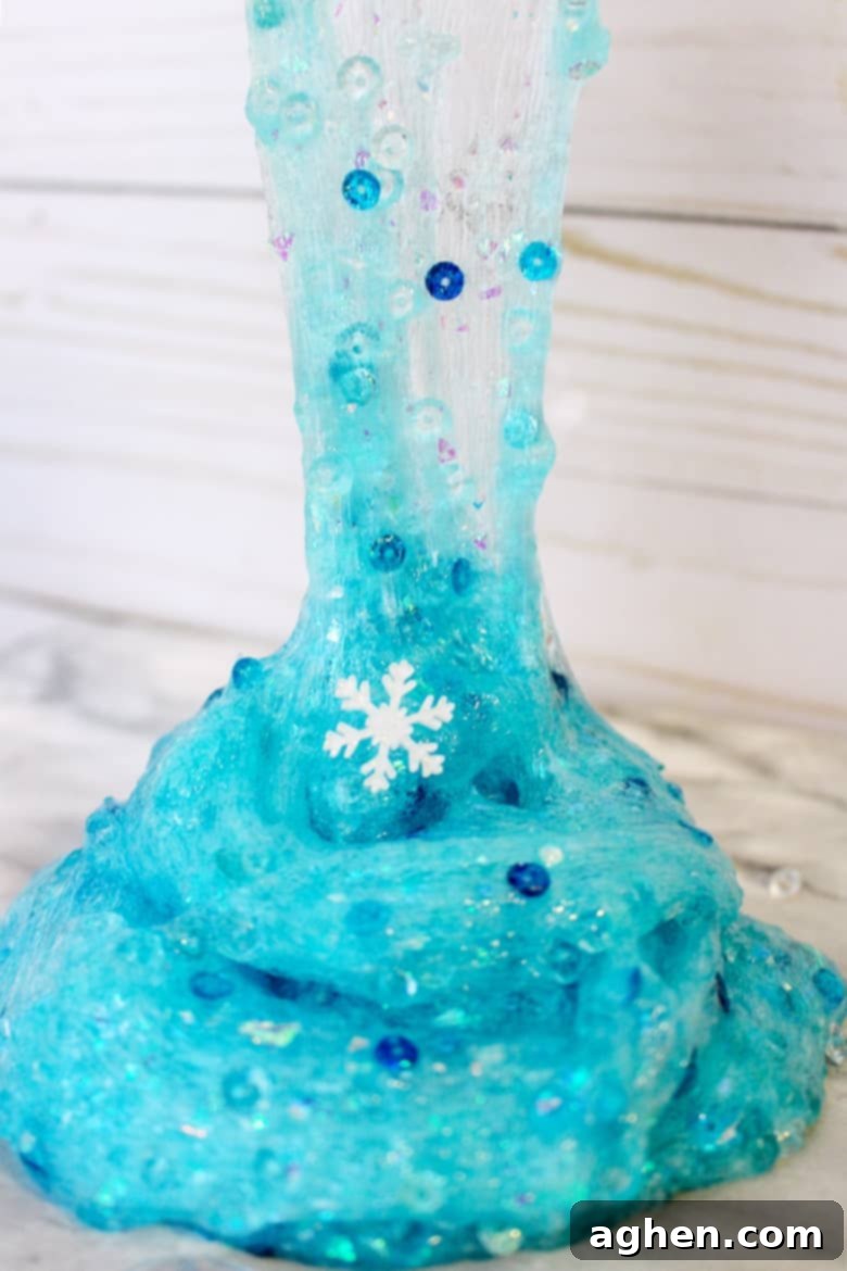 Close-up of sparkling blue Elsa-themed slime with snowflake and diamond beads, stretched by hands