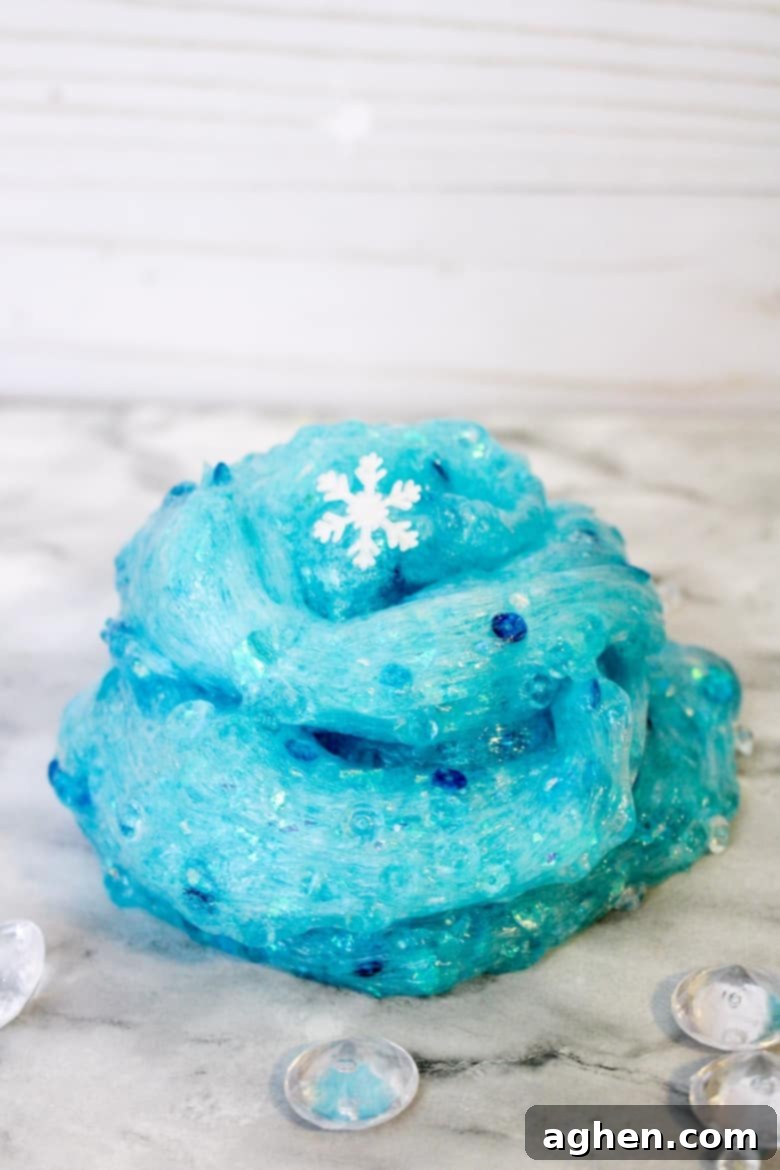 A close-up of handmade Frozen-themed slime with glitter and snowflake charms, being stretched over a marble surface