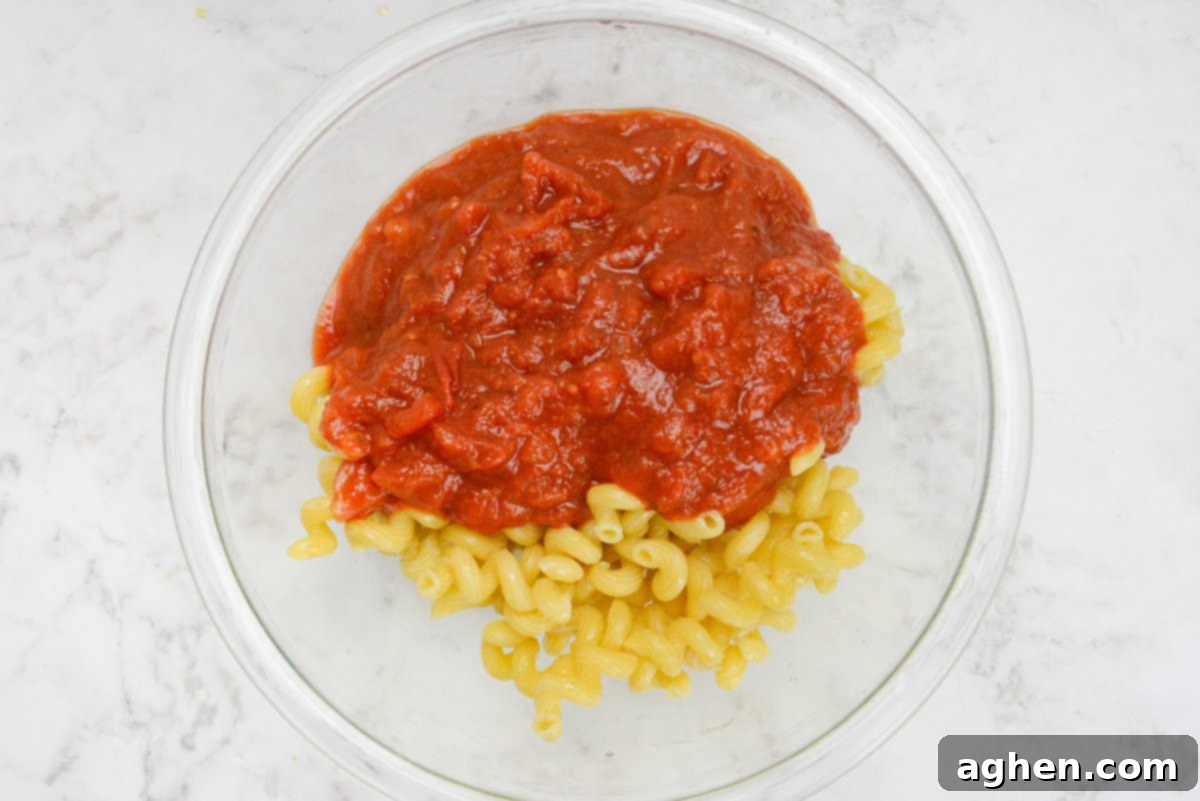 A large mixing bowl with the drained pasta and marinara poured on top but unmixed.