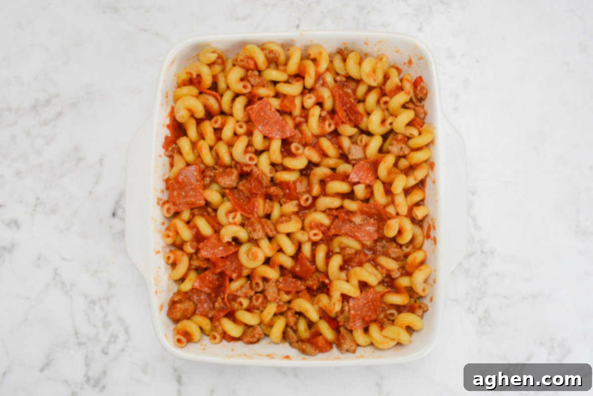 A white square casserole dish is filled with the pizza casserole ingredients 