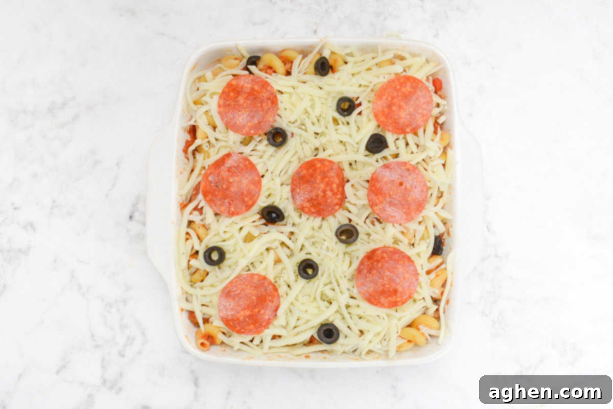 A white square casserole dish topped with cheese and whole slices of pepperoni and scattered sliced olives 
