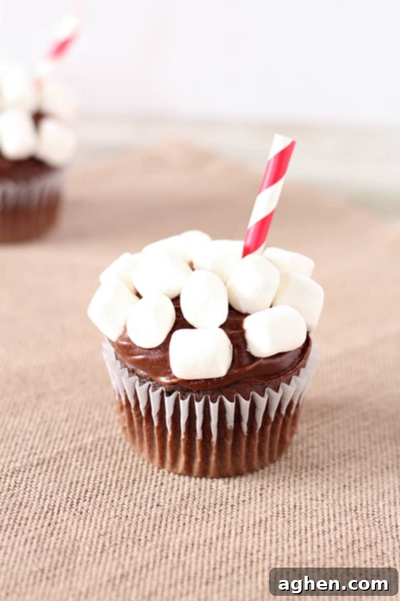 Delicious hot chocolate cupcakes arranged like a warm drink, topped with chocolate fudge icing and mini marshmallows, with a striped straw inserted.