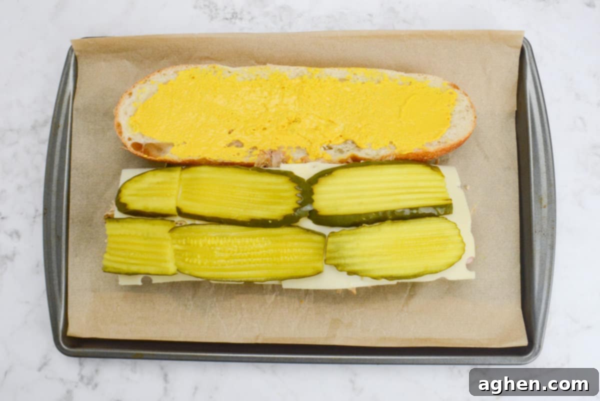 Öğle Yemeğiniz Asla Aynı Olmayacak: Blackstone Küba Sandviçi 8 Pickle slices carefully placed on top of the Swiss cheese in the Blackstone Cuban Sandwich construction.