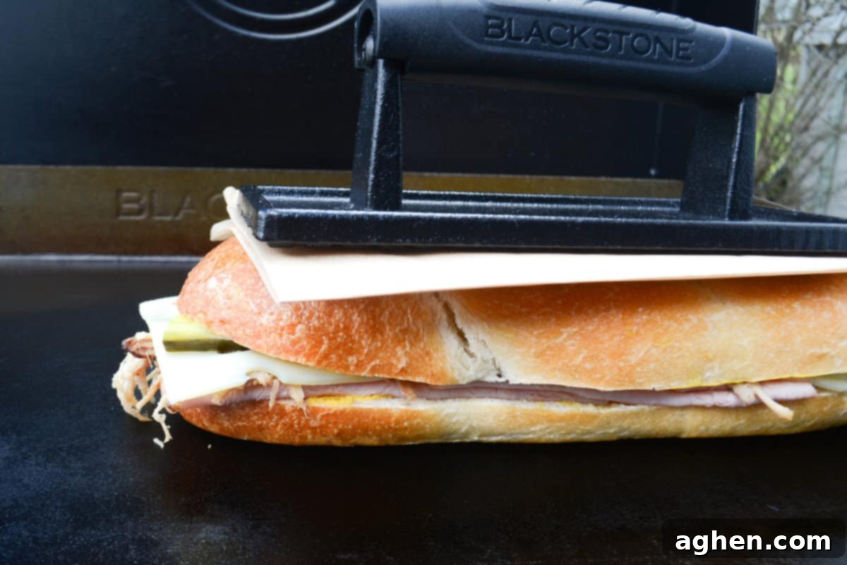 Öğle Yemeğiniz Asla Aynı Olmayacak: Blackstone Küba Sandviçi 10 Cuban sandwich cooking on Blackstone griddle, being pressed down firmly by a griddle press to flatten and toast.