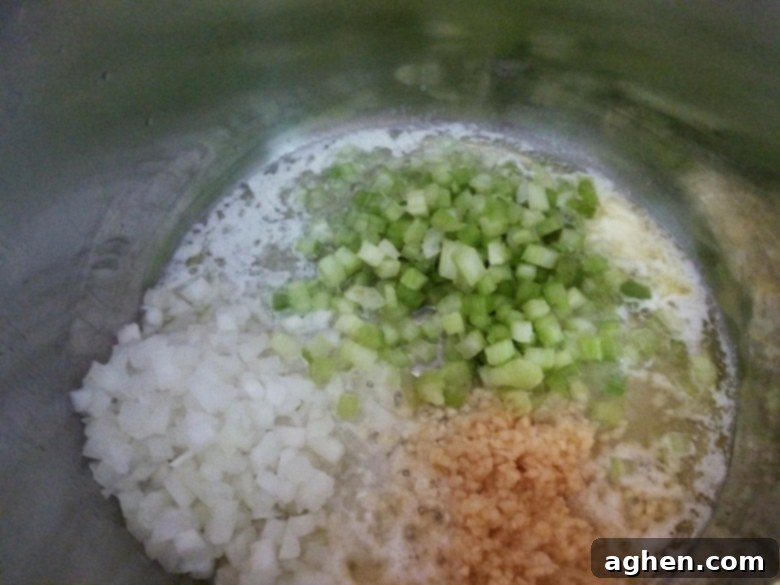 Diced onions, celery, and minced garlic lightly sautéing in butter and olive oil in the inner pot of a pressure cooker, releasing fragrant aromas.