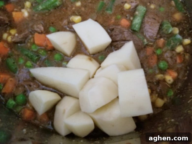 Adding perfectly cubed russet potatoes into the Instant Pot, joining other beef stew ingredients before the lid is sealed.