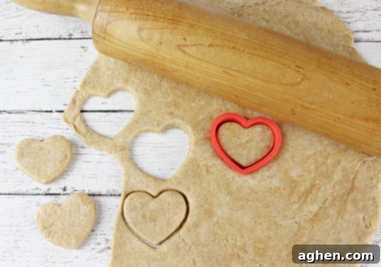 Dog treat dough rolled out with few heart shaped treats cut out. The rolling pin and cookie cutter are on top of the dough.