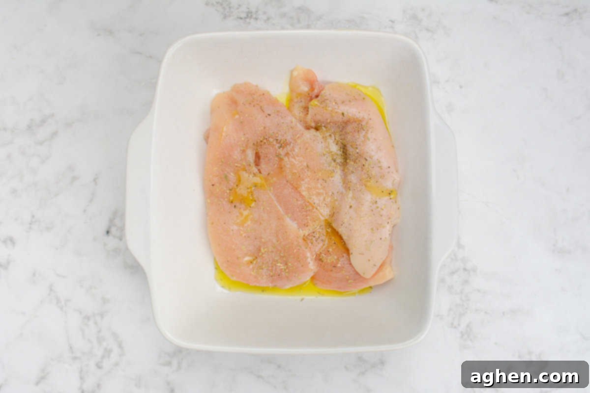 Effortless Delicious Weight Watchers Greek Sheet Pan Chicken 4 A square dish with raw chicken covered in olive oil, salt, oregano and pepper