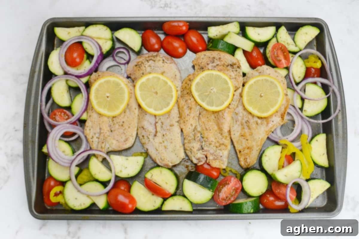 Effortless Delicious Weight Watchers Greek Sheet Pan Chicken 8 The assembled sheet pan meal ready for baking. The vegetables surround the seared chicken which is topped each with one lemon slice