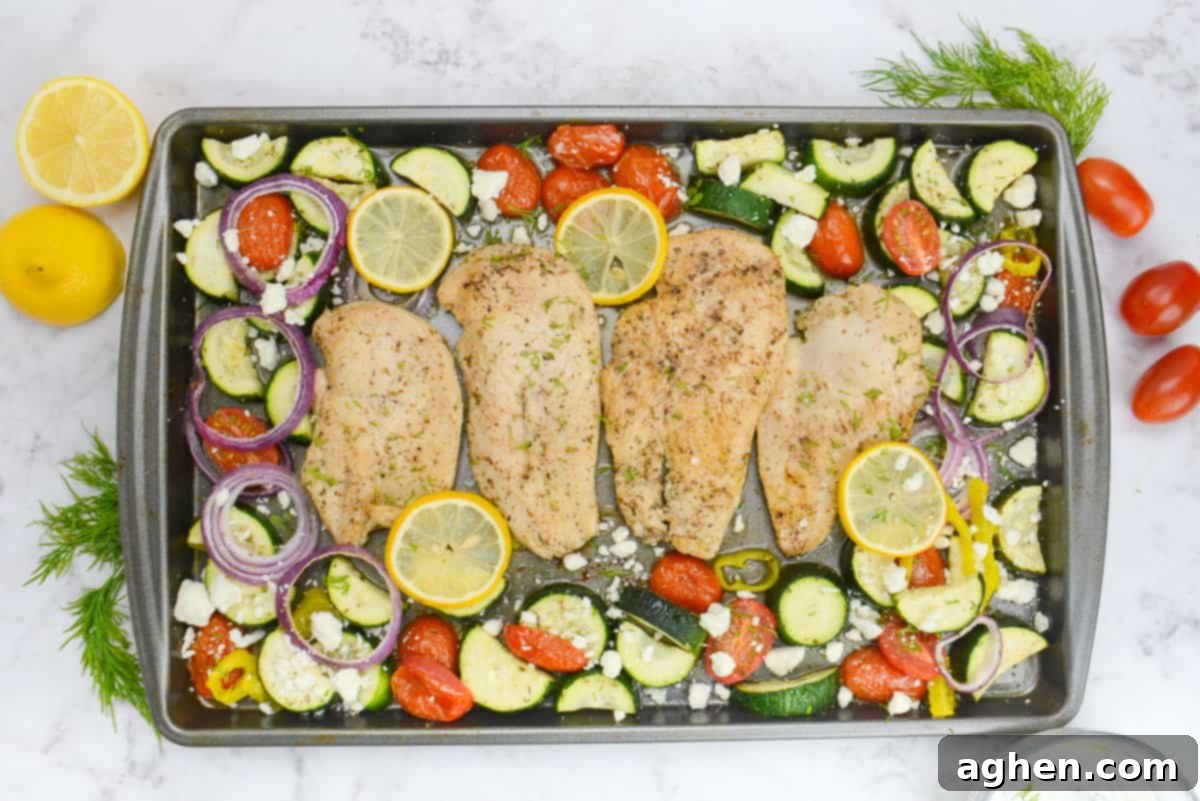 Effortless Delicious Weight Watchers Greek Sheet Pan Chicken 9 The finished Greek sheet pan meal. The chicken is surrounded by vegetables and topped with feta. To the side of the sheet pan sit a bowl of tzatziki, cherry tomatoes, dill and a cut lemon