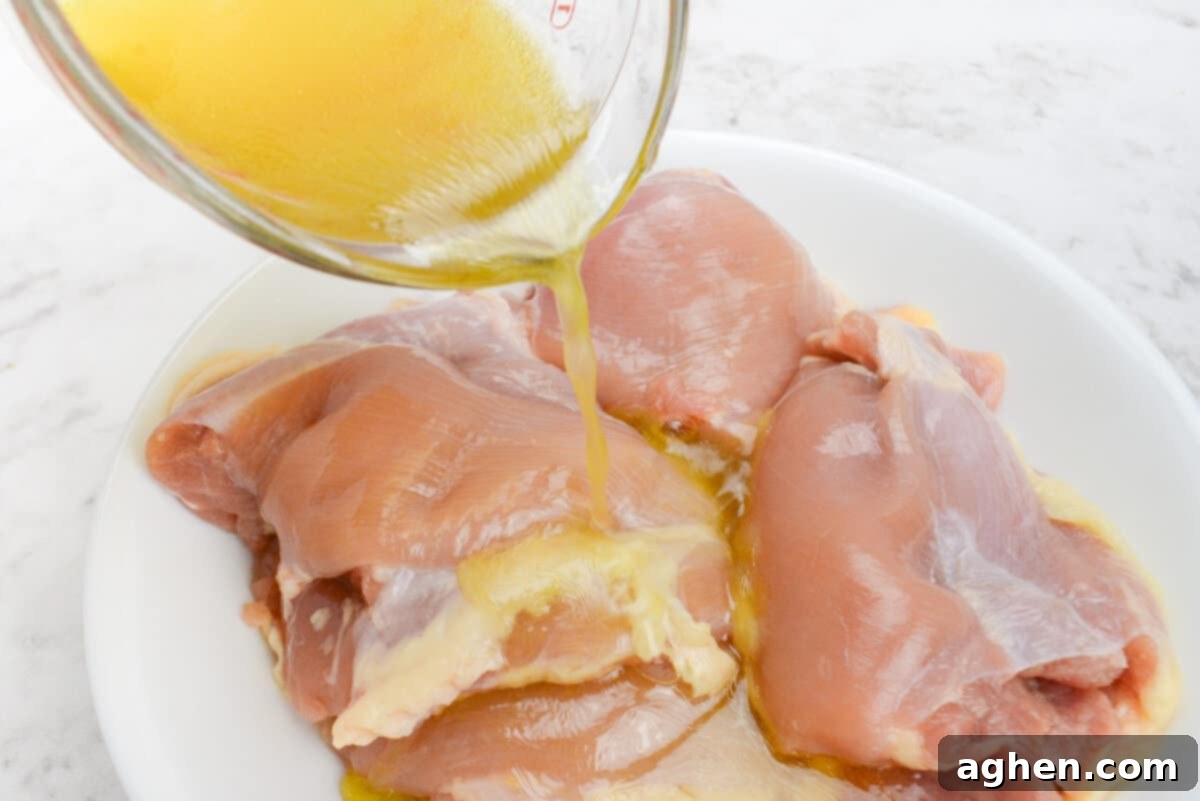 The measuring cup pours yellow liquid over the raw chicken thighs
