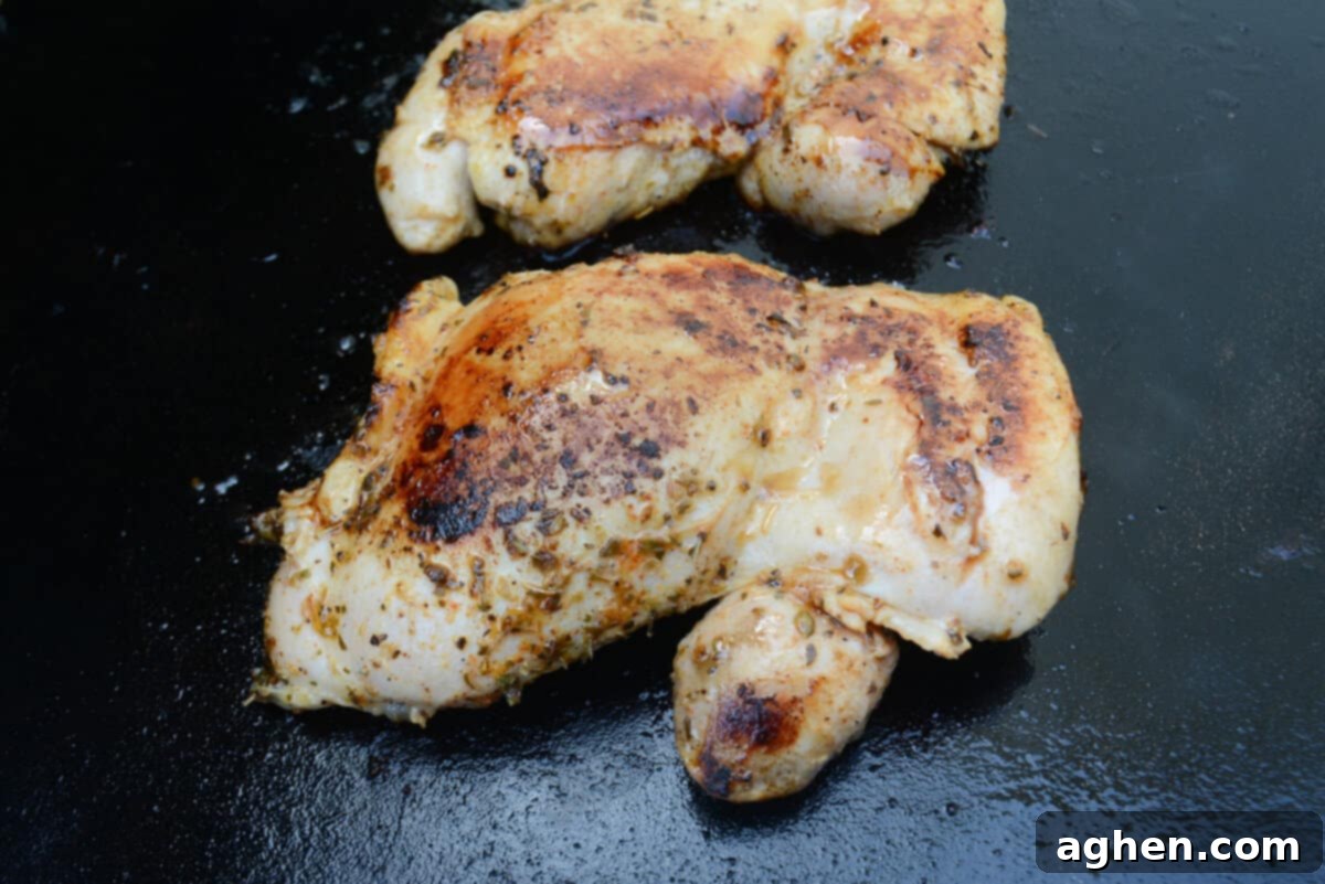 Close up of one browned and cooked thigh on the Blackstone with another sitting directly above.