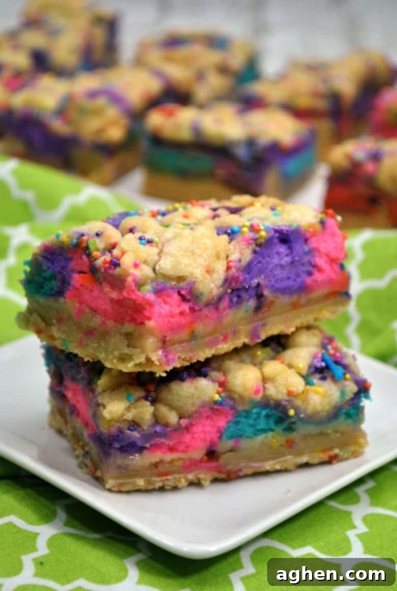Close-up of a stack of two unicorn bars, showing the distinct pink, purple, and blue cheesecake layers and a crumbly sugar cookie top.