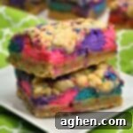 Two colorful layered dessert bars with bright pink, purple, and blue cheesecake swirls and cookie crumbles on top.