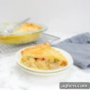 Single slice of Weight Watchers Chicken Pot pie sits on top of a white plate next to a grey napkin. In the background is a cooling rack with the casserole dish and a large spoon.