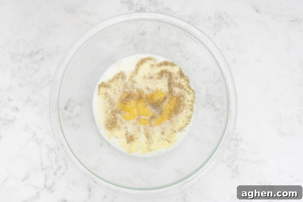 A large clear bowl showcasing the unmixed liquid ingredients for the pot pie filling: milk, seasonings, and yellow condensed soup.