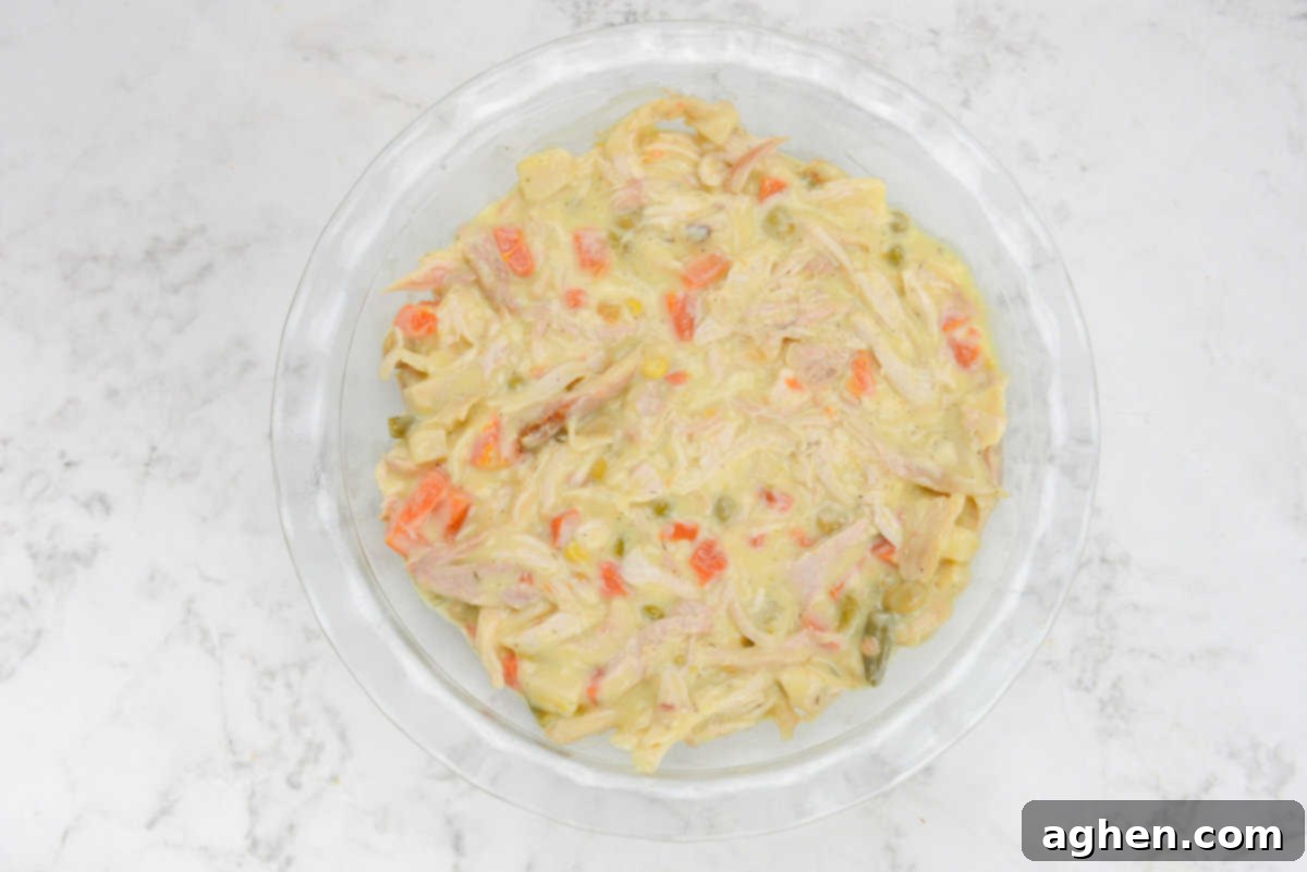 A clear glass pie pan filled with the savory chicken and vegetable mixture, spread evenly.