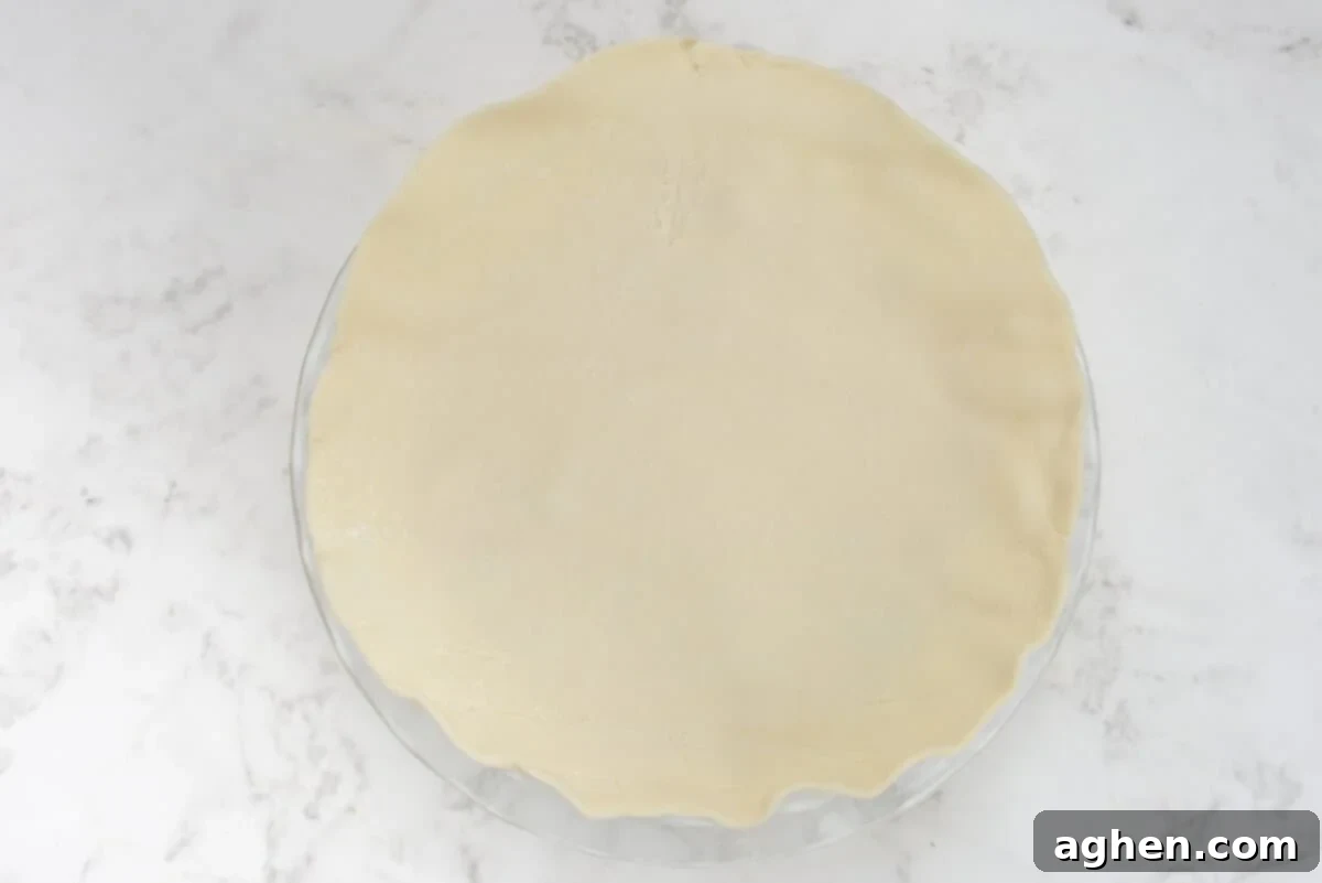 The unrolled pie crust gracefully draped over the pie pan, covering the chicken pot pie filling.