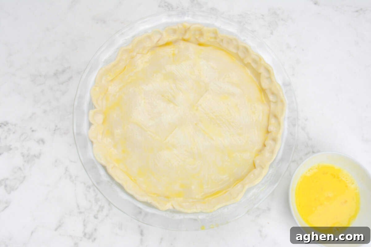 The assembled chicken pot pie, ready for the oven, with a glistening yellow egg wash coating the top crust.