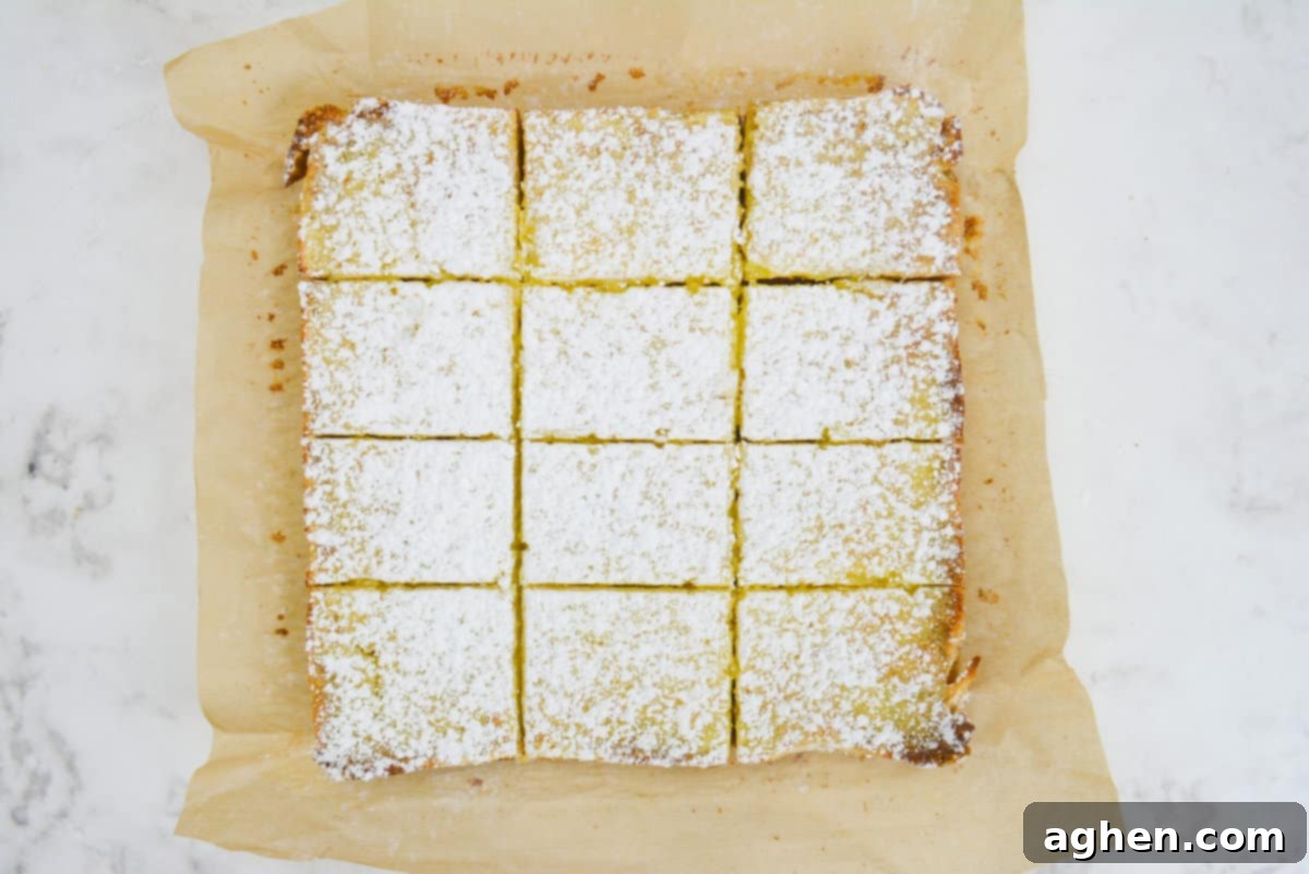 The finished bars topped with powdered sugar shown sliced into 12 equal bars on top of brown parchment 