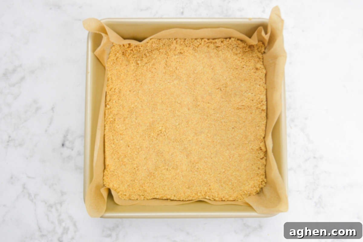 A gold square baking pan. The pressed crust sits in the pan while the brown parchment hangs slightly over the sides