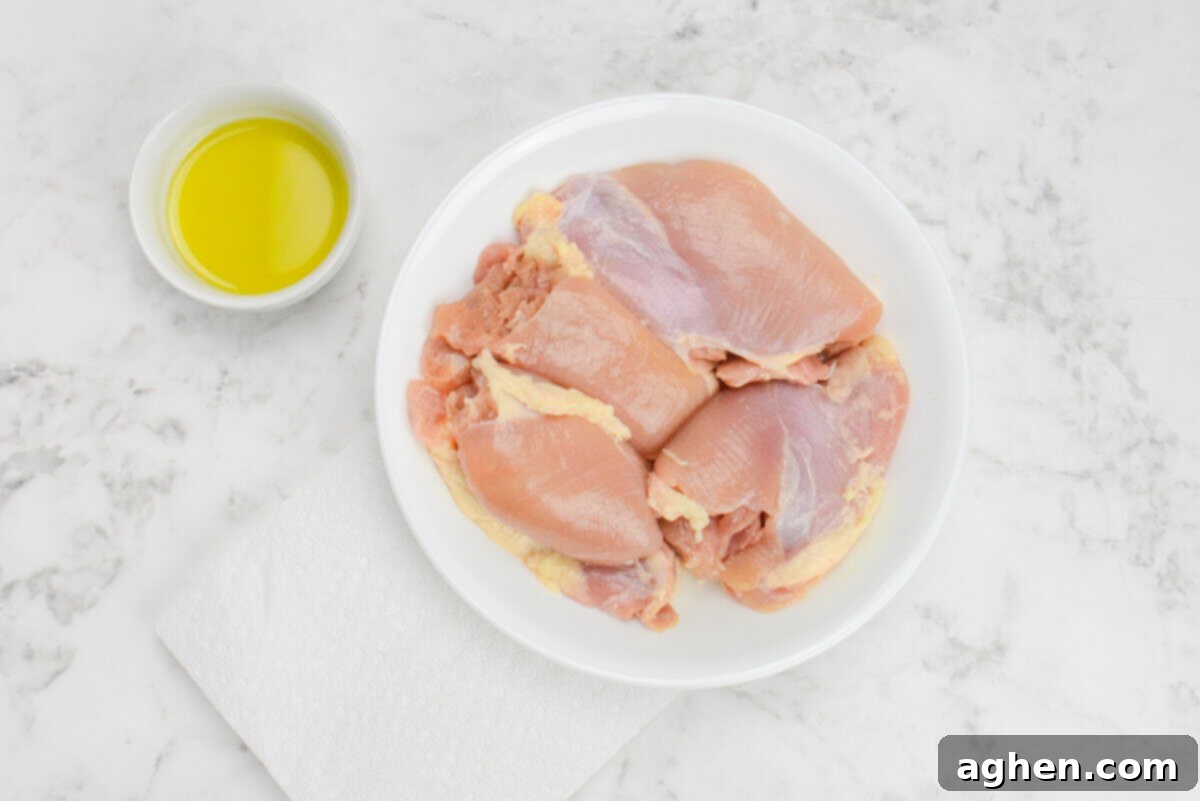 A plate of raw chicken thighs. To the side sides a small bowl of olive oil and a folded paper towel