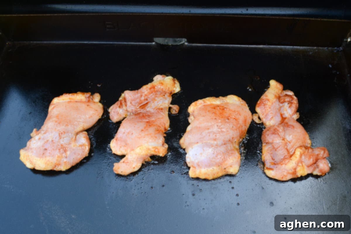 Four raw chicken thighs sit on the griddle