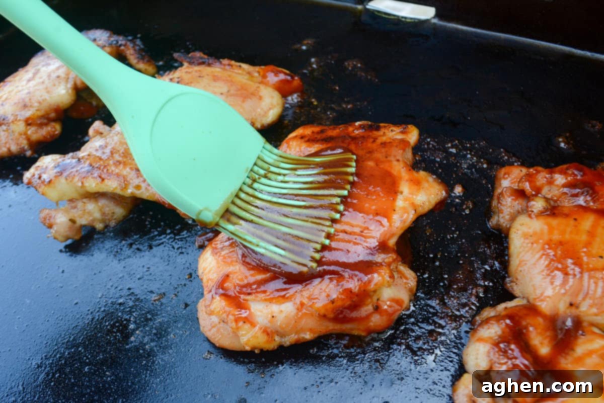 Close up of a green pastry brush adding sauce to the cooked chicken thigh 