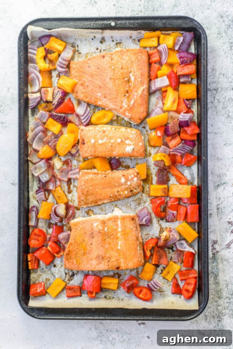 Chili lime salmon and assorted vegetables spread out on a sheet pan, ready for the oven.