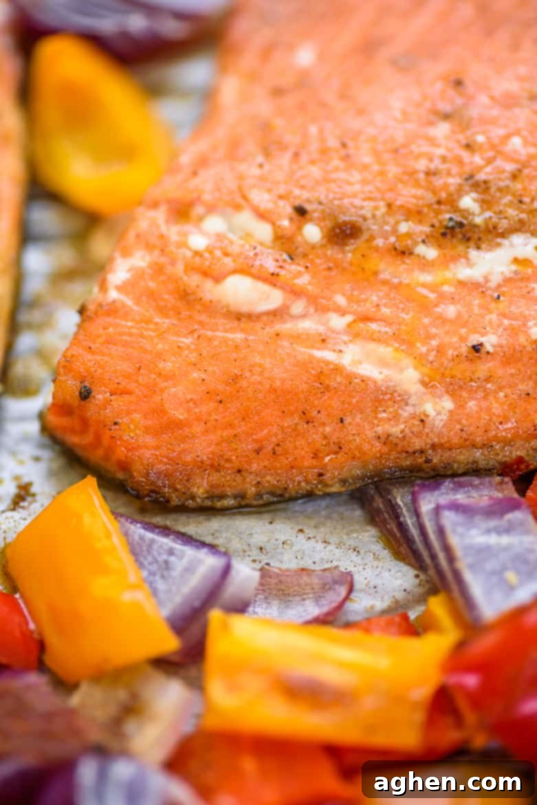 Close-up of a chili lime salmon fillet with roasted peppers and onions on a sheet pan, freshly out of the oven.