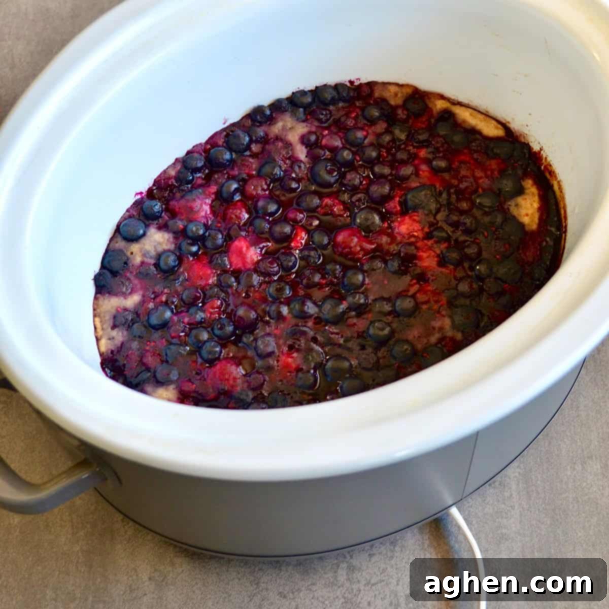 Mixed berry cobbler actively cooking and bubbling inside a slow cooker.