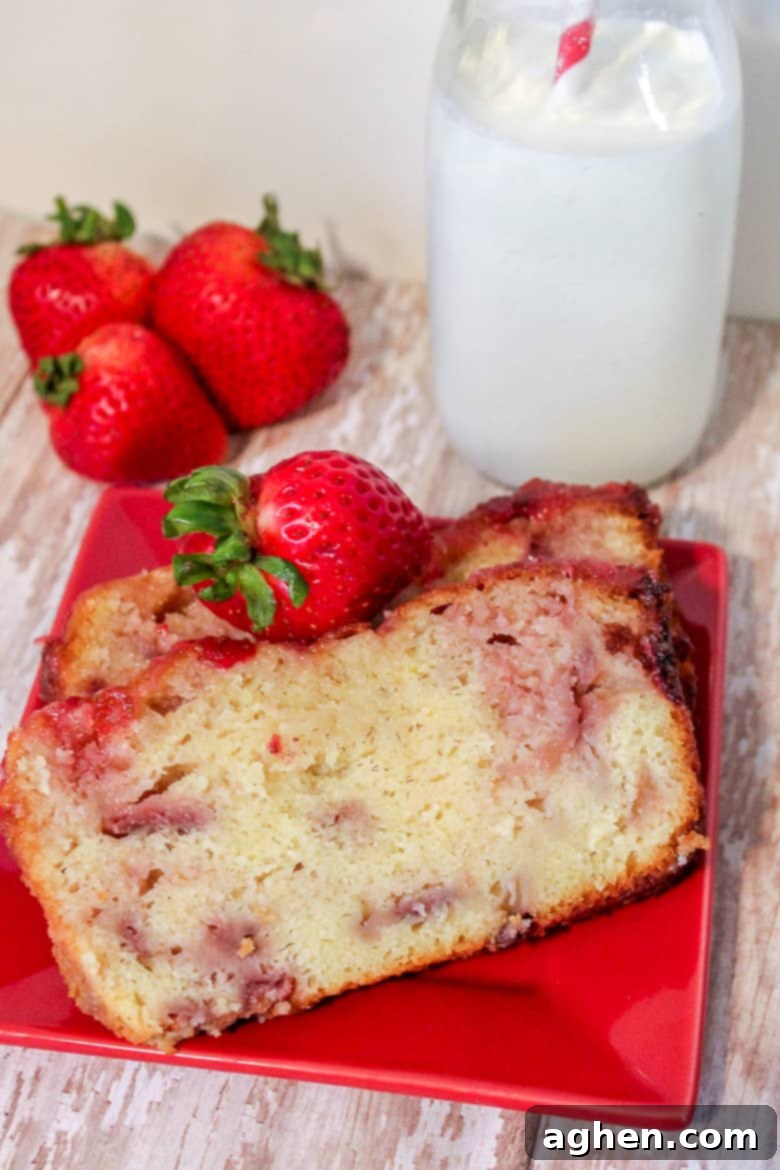 Two slices of strawberry yogurt pound cake on red plate with fresh strawberries.