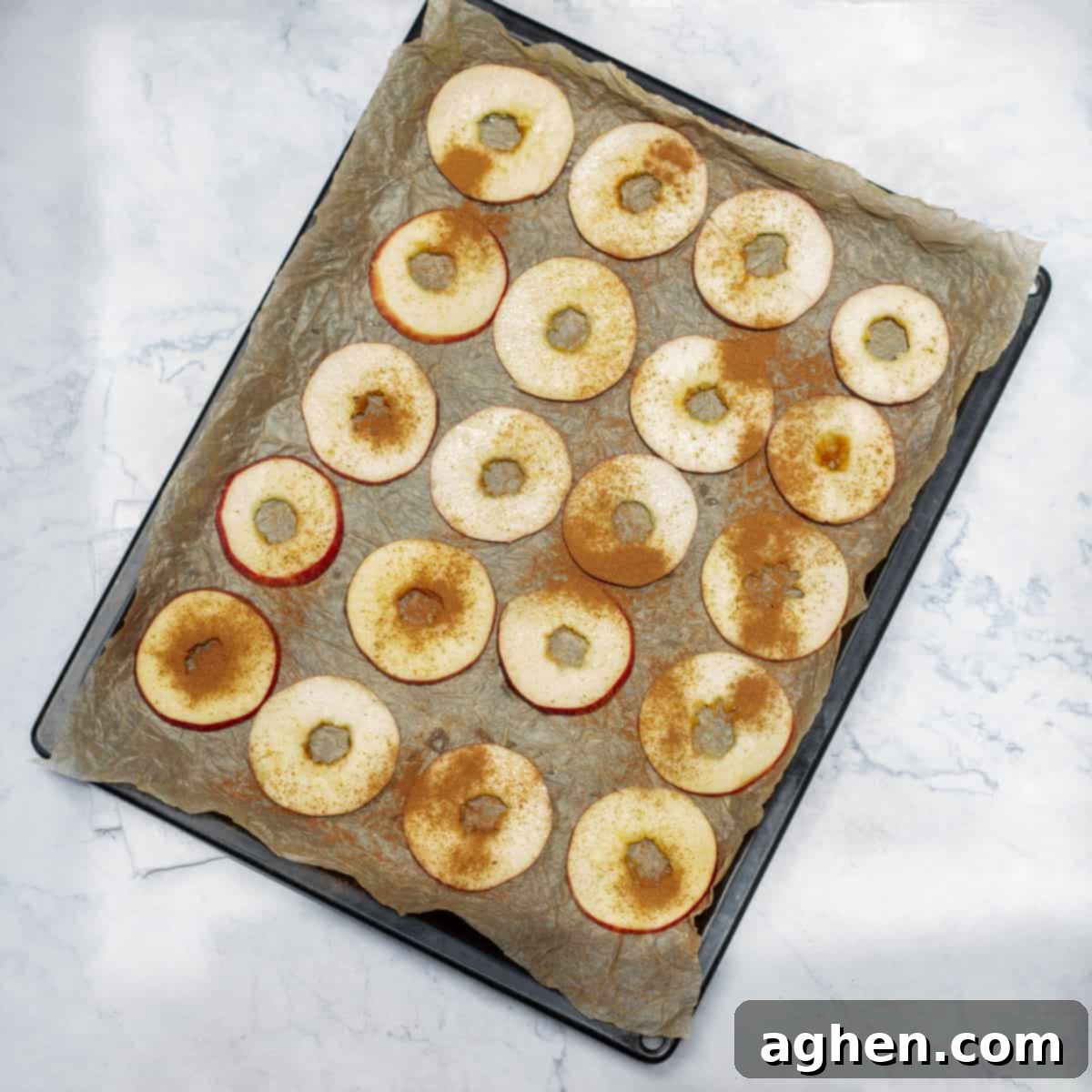 Seasoned apple slices arranged in a single layer on a baking tray lined with parchment paper