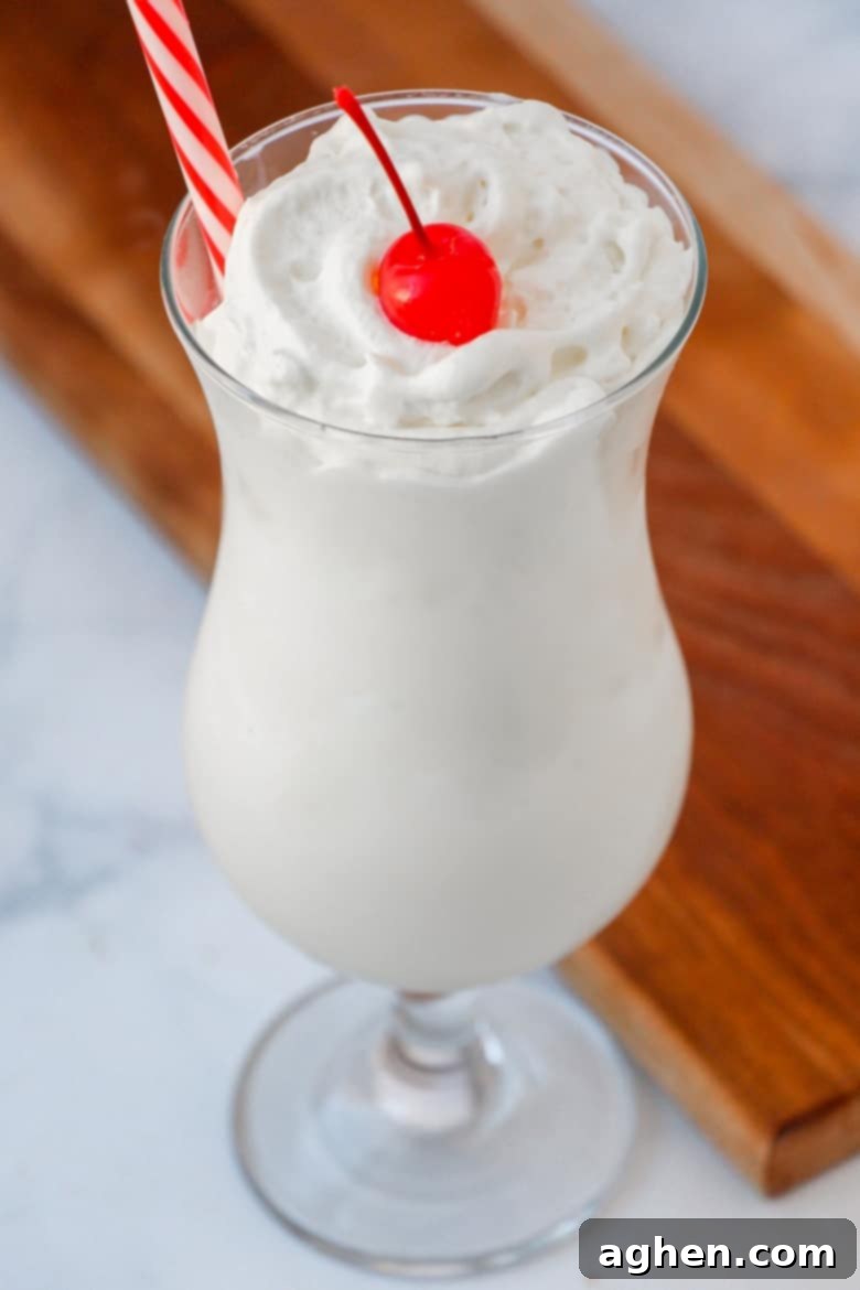 Vanilla frozen drink in a clear glass with a cherry on top and a straw.