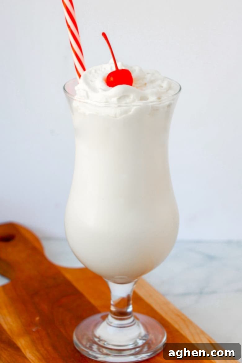 Vanilla frozen drink in a clear glass with a cherry on top and a straw.