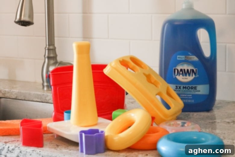 A collection of plastic toys on a kitchen countertop next to a bottle of Dawn dish soap, ready for cleaning